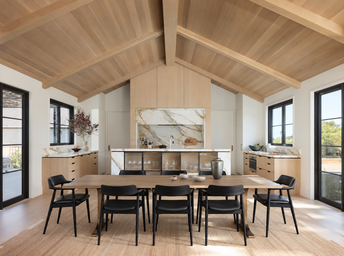Certainly! Here is a rewritten version of the sentence, incorporating your product data: A modern kitchen and dining area featuring wood ceilings, a striking SOBU Mars Live Edge Dining Table in white ash with brass T legs as the centerpiece, surrounded by six black chairs, marble accents, large windows, and neutral-toned cabinetry.
