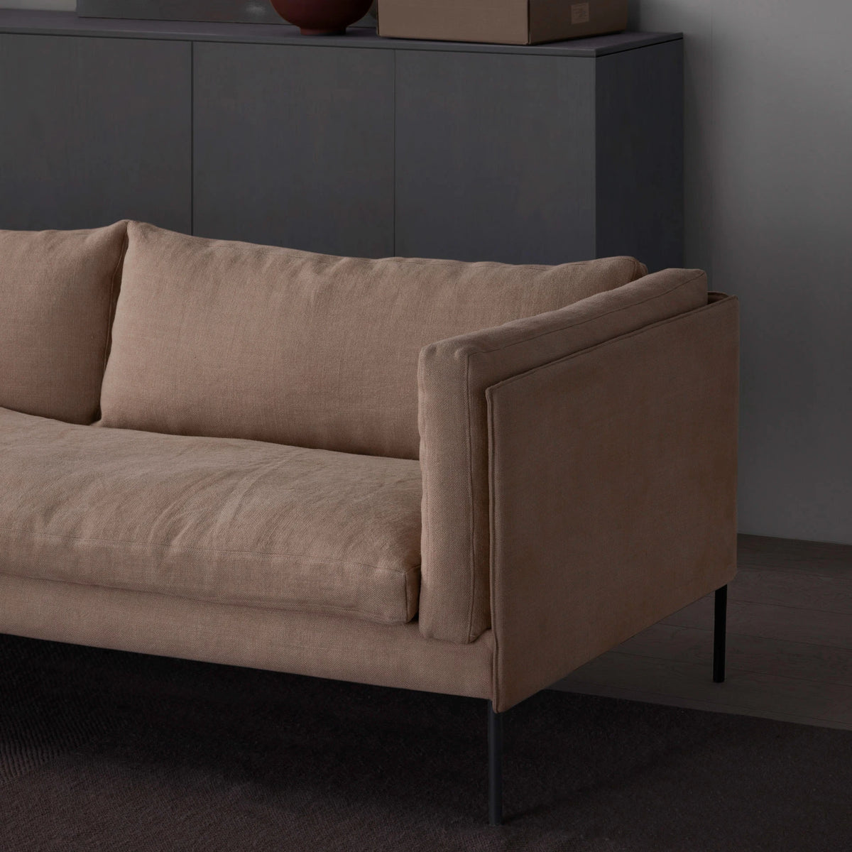 A tan Sonder Sofa | Fabric with slim metal legs positioned in front of a dark storage cabinet.