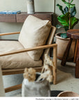 The Troubadour Lounge Chair | Leather by Wooden Stories in light tan leather and walnut sits beside a potted plant, wooden stool, and console table to create a cozy, modern living space.