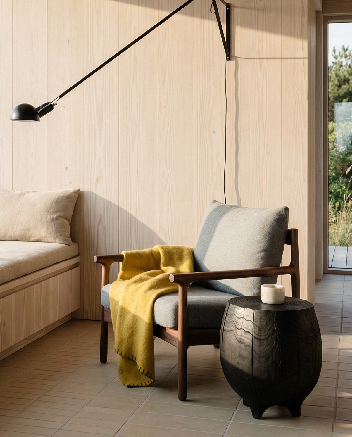 A cozy modern room with large windows, a wood-paneled wall, a cushioned bench, the SOBU Viking Lounge Chair in walnut with a mustard yellow throw, a small side table, and a black wall lamp. Natural light fills the space.