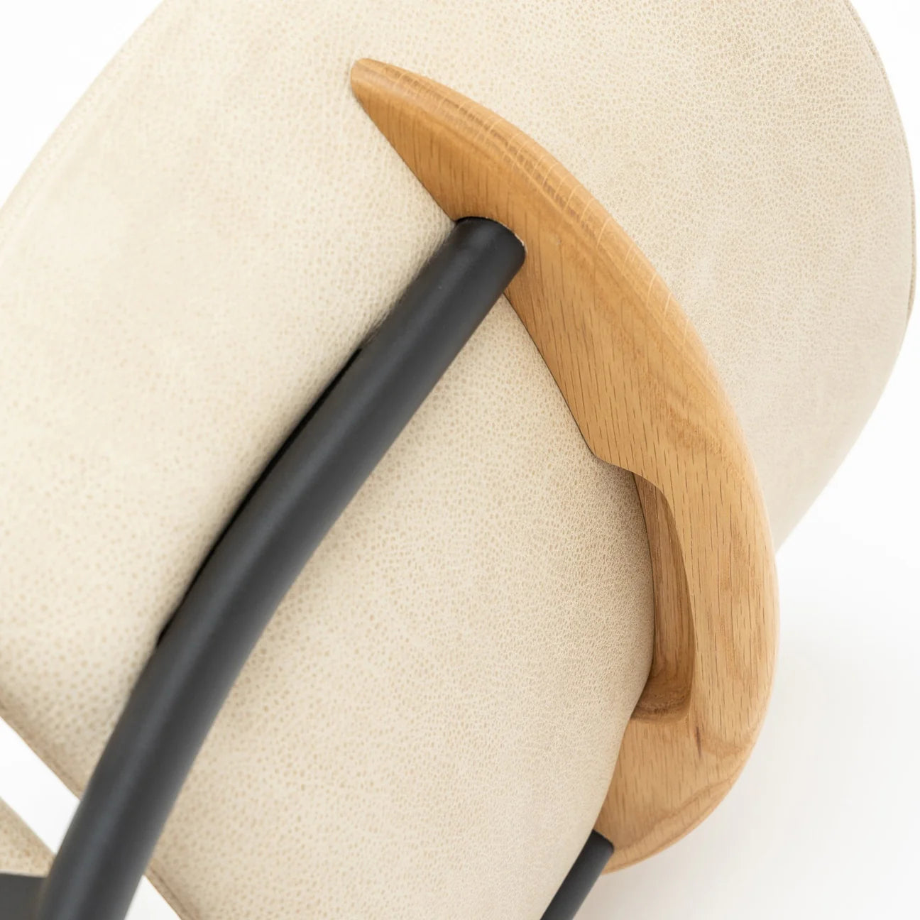 Close-up of the Solace Dining Chair | Leather by Wooden Stories—an upholstered chair with a light beige backrest, curved solid wood handle, and black metal frame shown against a white background.