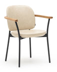 The Solace Dining Armchair | Leather by Wooden Stories features a modern beige upholstered seat and backrest, black metal legs, and wooden armrests, shown against a plain white background.