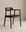 The SOBU Sven Dining Chair features a sleek black ash frame with a curved backrest, leather seat, armrests, and four straight legs. Styled against a plain beige background, this modern chair blends comfort and elegance.