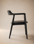 The SOBU Sven Dining Chair in black ash features armrests, a curved backrest, and sleek, modern lines. Shown in side profile against a beige background, it’s optionally upholstered in black Italian leather for a refined finish.