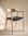 The SOBU Sven Dining Chair in White Ash and leather features a curved backrest, armrests, and a black cushioned seat, crafted with a natural finish and shown against a neutral beige background with soft lighting.
