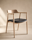 The SOBU Sven Dining Chair in White Ash and leather features a curved backrest, armrests, and a black cushioned seat, crafted with a natural finish and shown against a neutral beige background with soft lighting.