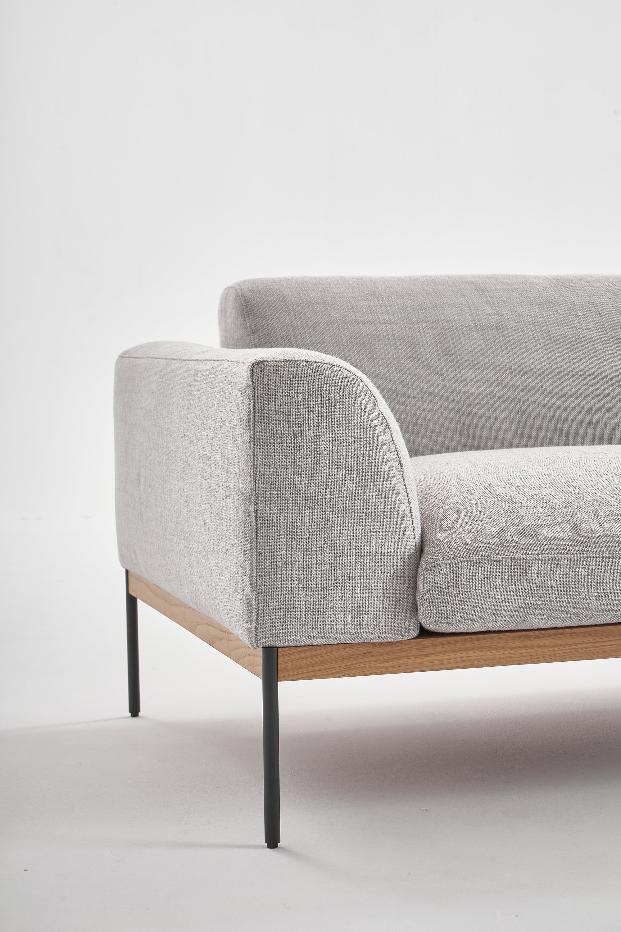 The Wooden Stories Department Sofa 93&quot; | Fabric is a modern light gray sofa with Danish-style lines, black metal legs, and a solid wood plinth. Shown against a white background, only one armrest and part of the seat are visible.