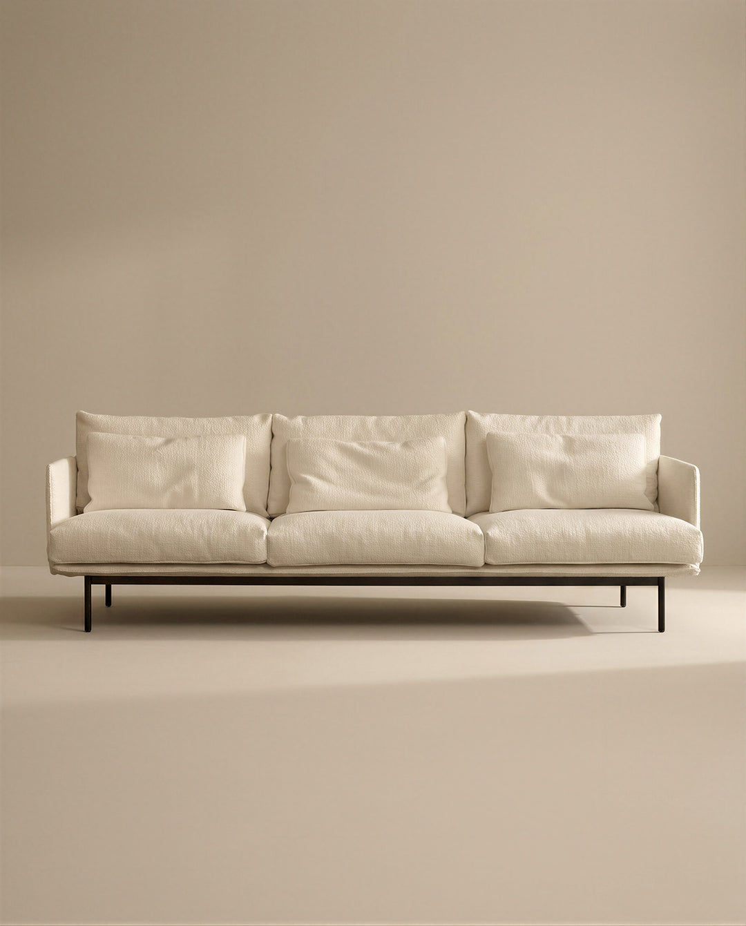 The Cherry Sofa | Fabric by SOBU is a modern cream 3-seater with Danish lines, three seat and back cushions, slim black metal legs, and a minimalist design—perfect for any contemporary living space. Plain beige background enhances its sleek look.