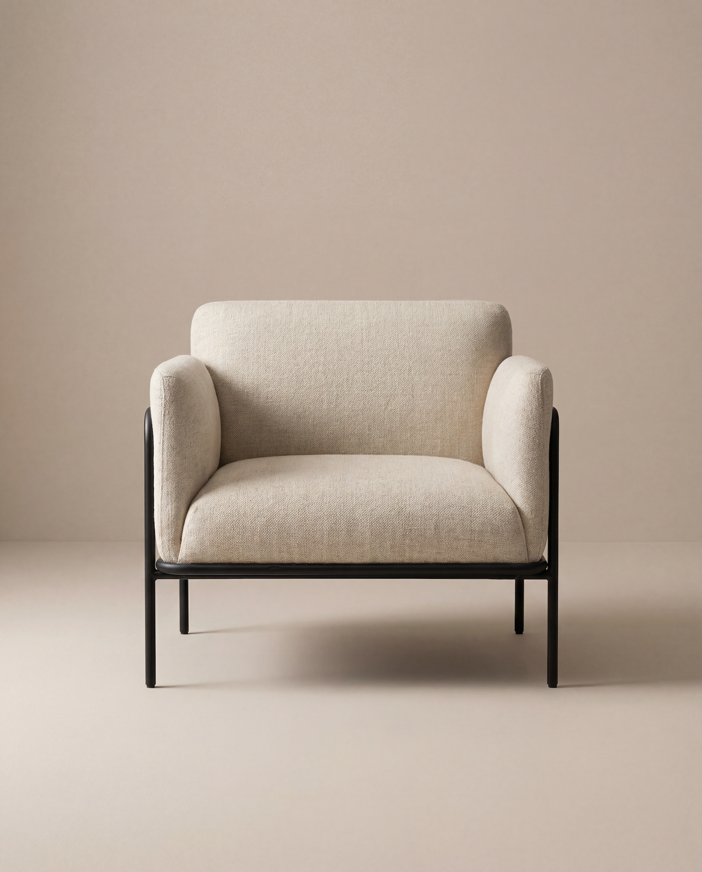 The Scribe Lounge Chair | Fabric by Wooden Stories features a contemporary design with beige upholstery, rounded armrests, and a sleek black metal frame, perfectly set against a neutral beige backdrop.
