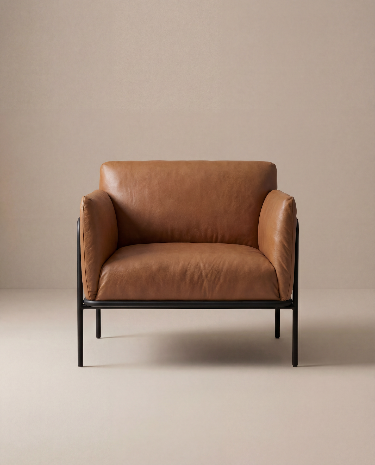 The Scribe Lounge Chair by Wooden Stories features tan leather upholstery and black metal legs, bringing Bauhaus-inspired contemporary style to life against a plain beige background.