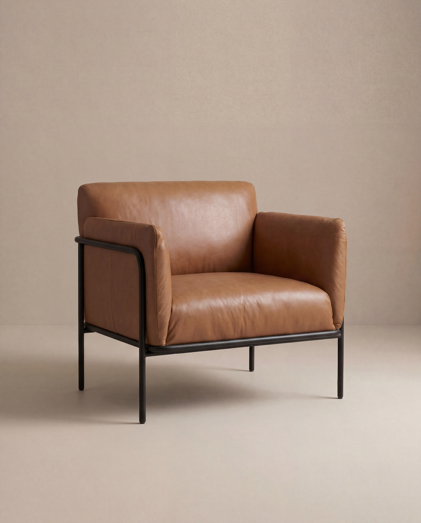 The Scribe Lounge Chair | Leather by Wooden Stories, featuring brown leather upholstery and a black metal frame, stands out in a minimalist space with beige walls and floors, showcasing its sleek, contemporary Bauhaus-inspired design.