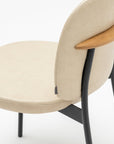 A close-up of the Solace Dining Chair | Leather by Wooden Stories, featuring a beige upholstered seat and backrest, black steel legs, and a curved wooden accent on the backrest, set against a plain white background.