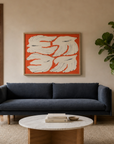 A modern living room featuring the Sonder Sofa | Fabric by Wooden Stories in navy, characterized by its slim proportions, paired with a wooden armchair, round coffee table, potted plant, and abstract art with orange and white accents on the wall. Large windows showcase trees outside.