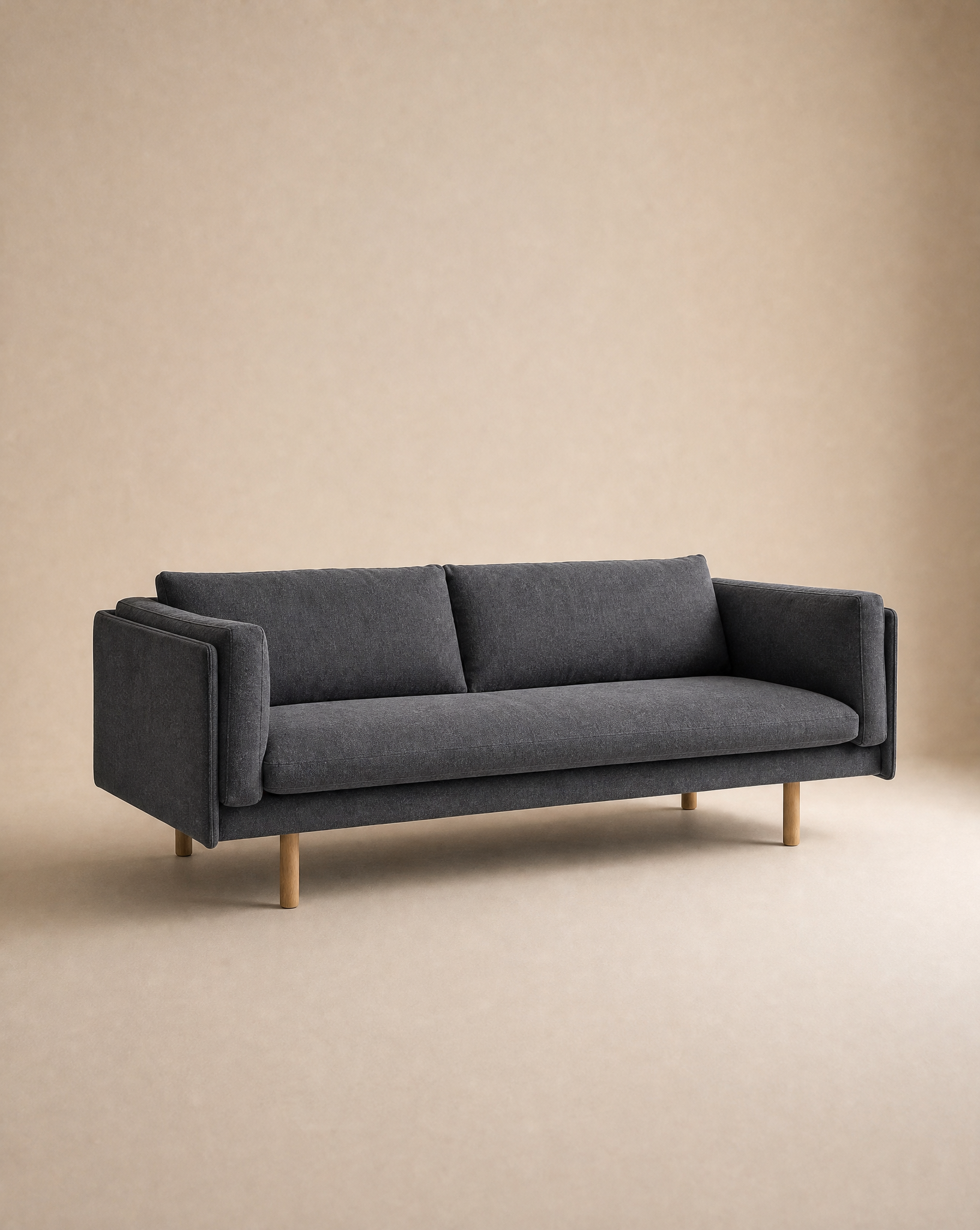 The Sonder Sofa | Fabric by Wooden Stories features a modern, minimalist design in dark gray, with two feather-filled cushions and wooden legs. Its clean lines, linear frame, and straight armrests create a sleek look, making it stand out against the neutral beige background.