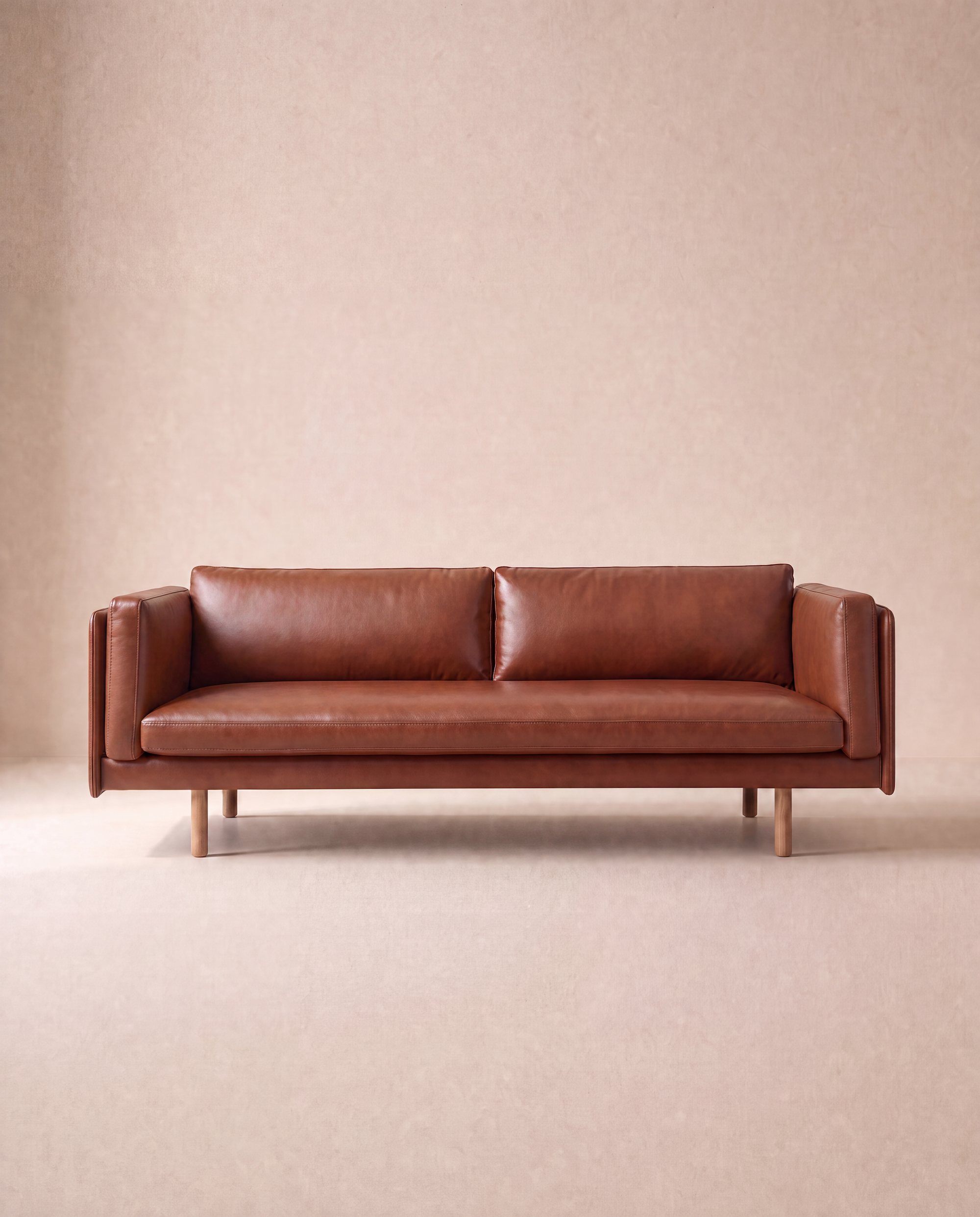 A modern brown Sonder Sofa | Leather by Wooden Stories is centered against a plain, light beige background. Inspired by Borge Mogensen, the sofa features a minimalistic, boxy design with wooden legs, two feather-filled seat cushions, and two back cushions.