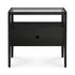 The Spindle Nightstand - Black Oak by Ethnicraft is crafted from solid European oak and features a glass top, an open shelf, a drawer with a round cut-out handle, and four slim legs for a modern look.