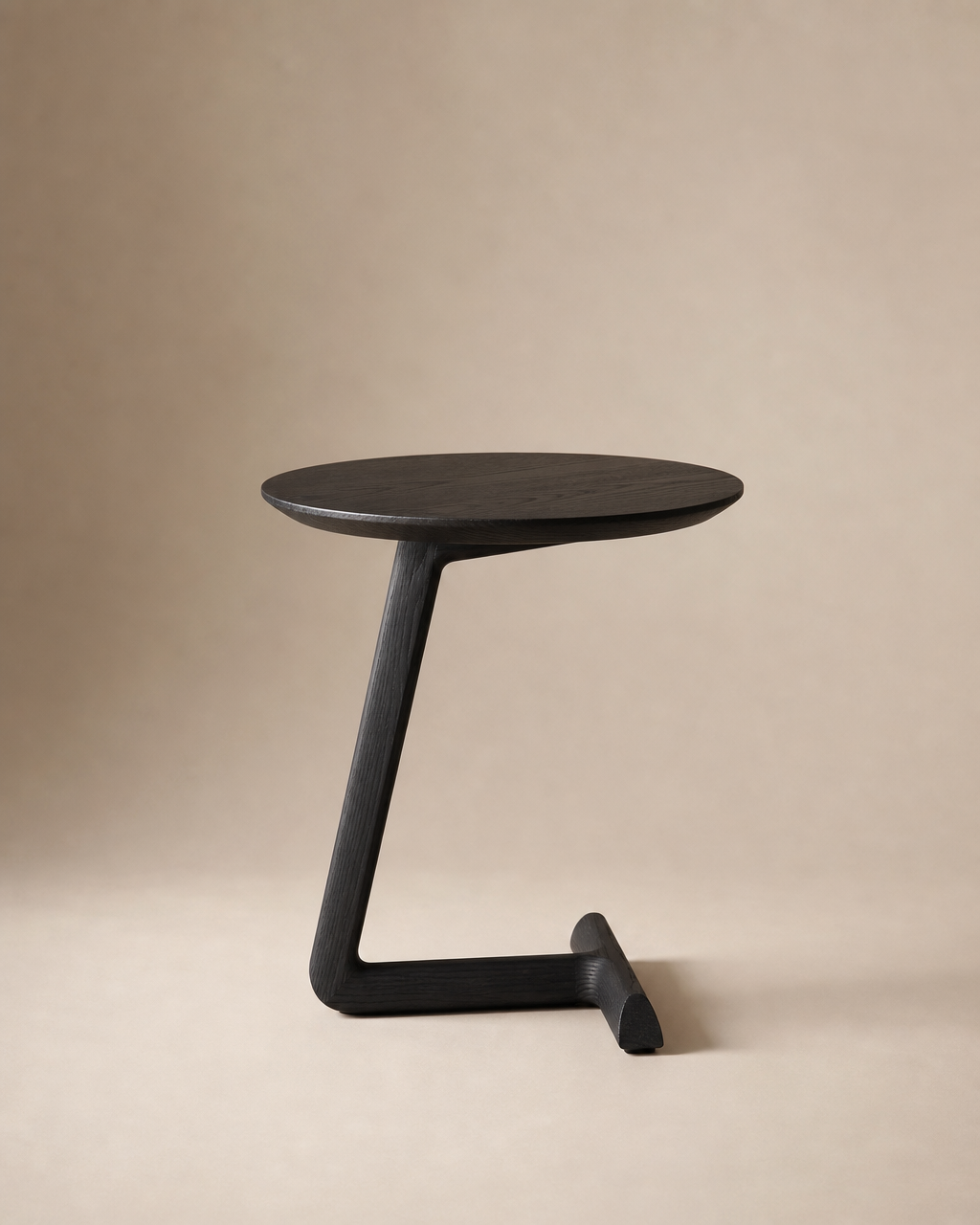 The SOBU Teena Side Table - Black Ash features a modern, minimalist design with a round black-stained ash top, single angled leg, and T-shaped base, shown in a compact form against a plain beige background.