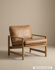 A modern Troubadour Lounge Chair | Leather by Wooden Stories, featuring a light oak wood frame and tan leather cushions, is set against a beige background. A small label at the bottom right reads Alabama Pecan with Light Oak.