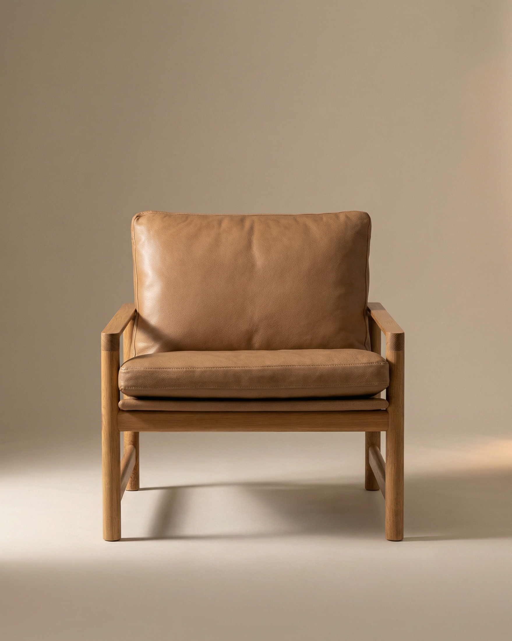 The Troubadour Lounge Chair | Leather by Wooden Stories features a solid oak frame and light brown leather cushions, set against a beige background with soft lighting. Inspired by Danish collections, it offers timeless elegance and comfort.