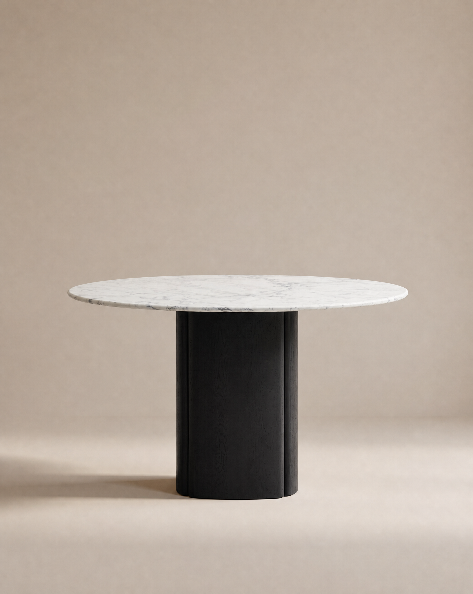 The Tathra Round Dining Table by Wooden Stories features a white marble top and thick black cylindrical base, built to contract grade standards, displayed against a plain beige background.