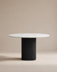 The Tathra Round Dining Table by Wooden Stories features a white marble top and thick black cylindrical base, built to contract grade standards, displayed against a plain beige background.