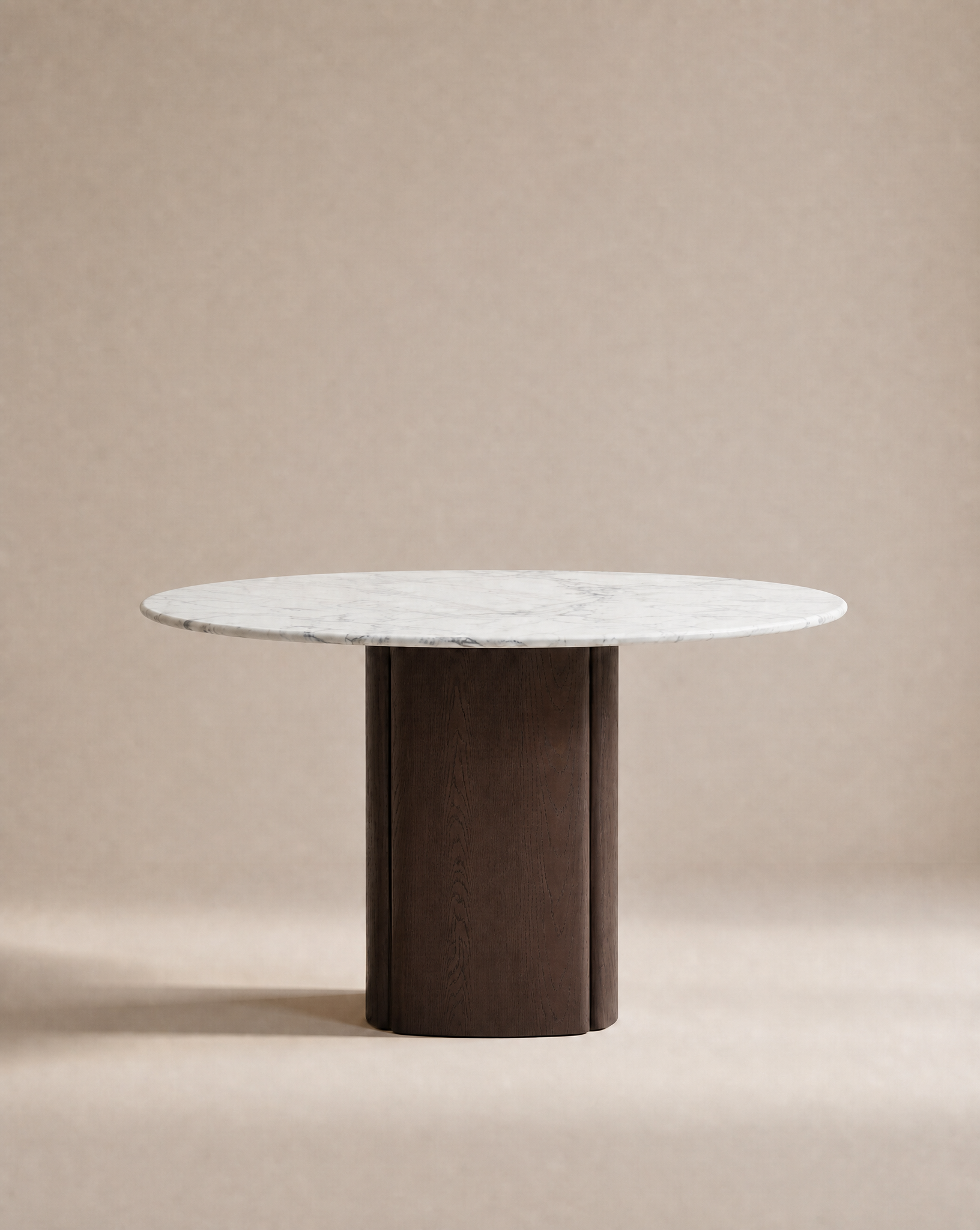 The Tathra Round Dining Table by Wooden Stories features a stone top and sturdy, cylindrical dark wood base, showcased against a neutral beige background.