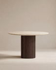 The Tathra Round Dining Table by Wooden Stories features a light stone top and a cylindrical dark solid oak base, shown against a plain beige background.