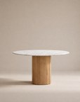 The Tathra Round Dining Table by Wooden Stories features a stone top and cylindrical solid oak base, showcased against a neutral beige background.