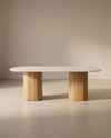 The Tathra Ellipse Dining Table by Wooden Stories features a smooth oval stone top and twin cylindrical wooden bases, exemplifying European craftsmanship and modern design—perfect for minimalist, neutral-toned spaces.