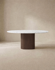 The Tathra Round Dining Table | Stone Top by Wooden Stories features a white marble top and wide solid oak pedestal base, set against a neutral beige background. Its minimalist, modern design is contract grade for lasting durability.