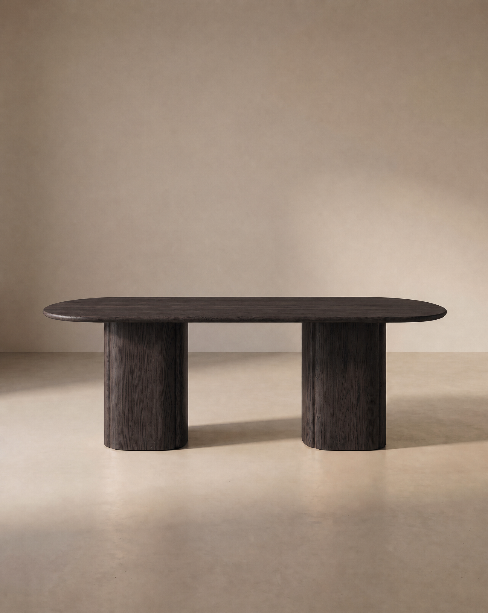 The Tathra Ellipse Dining Table by Wooden Stories, crafted from dark oak with two substantial cylindrical legs and an elegant oval silhouette inspired by classic Danish design, is showcased against a plain beige background.