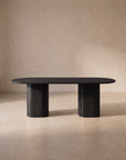 A modern oak Tathra Ellipse Dining Table by Wooden Stories, featuring two cylindrical pedestal legs, sits in a neutral, softly lit room with a plain beige background, embodying the timeless elegance of Danish design.