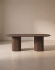 The Tathra Ellipse Dining Table by Wooden Stories features a modern oval shape crafted from oak, reminiscent of Danish design, with a smooth surface and two cylindrical pedestal legs, elegantly set against a neutral beige background.