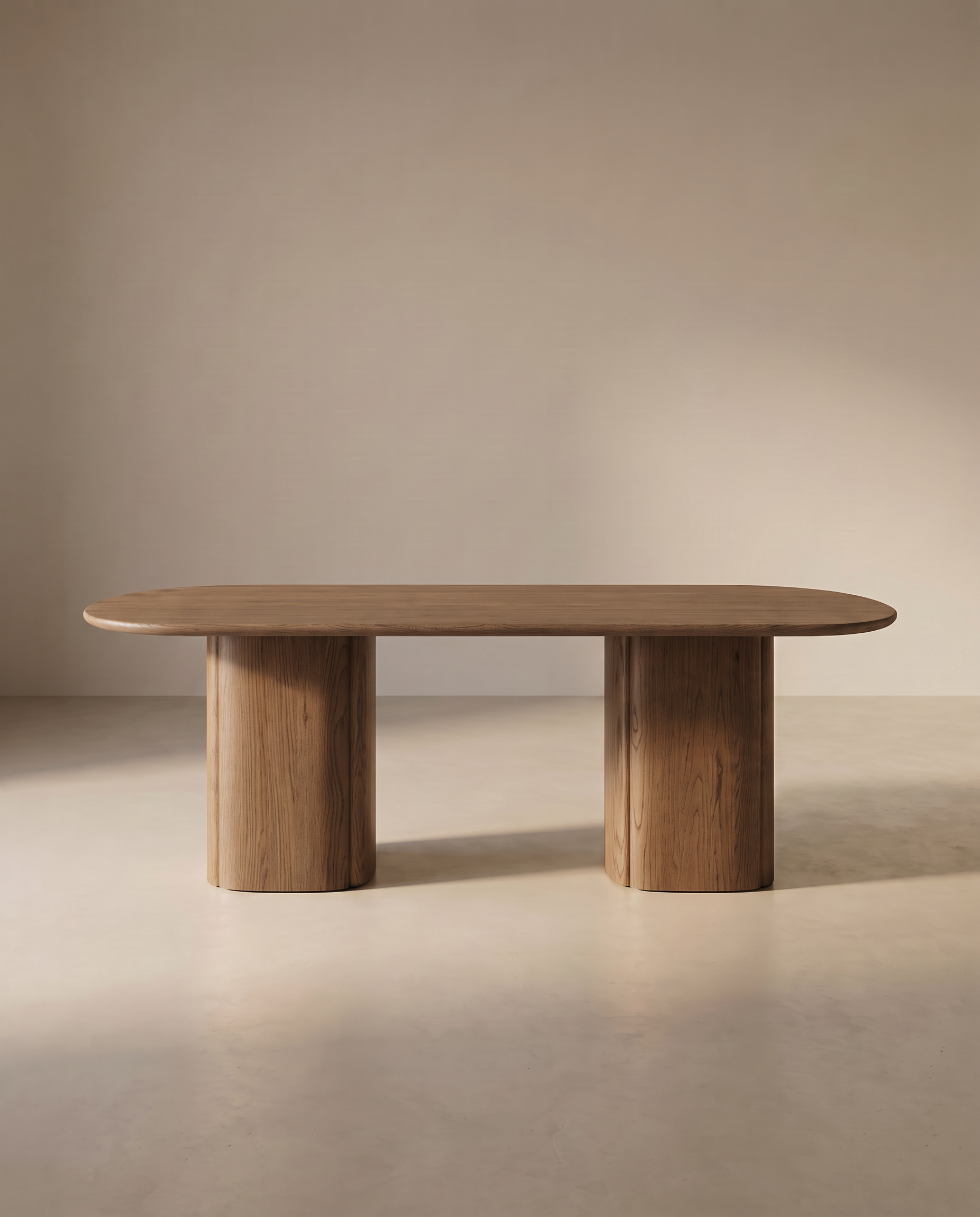 The Tathra Ellipse Dining Table | Oak by Wooden Stories features a modern solid oak oval top and two wide cylindrical legs, beautifully displayed in a minimalist room with neutral walls and flooring.