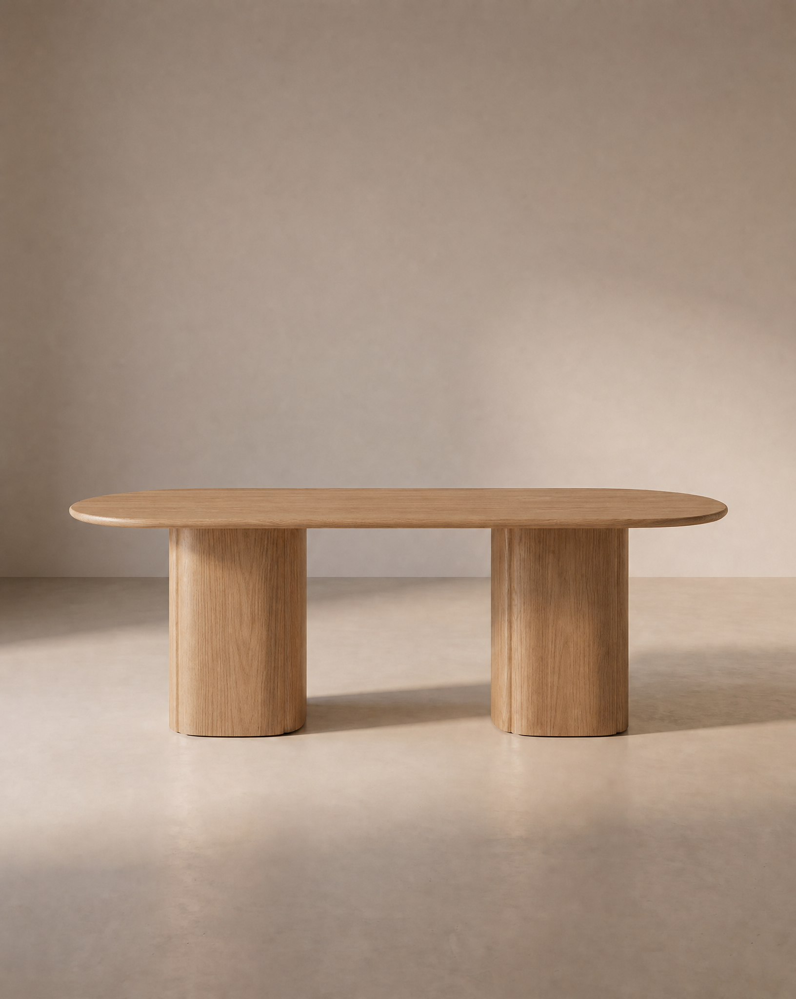 The Wooden Stories Tathra Ellipse Dining Table | Oak features a minimalist solid oak design with a smooth oval top and two cylindrical pedestal legs, elegantly situated in a softly lit, neutral-toned room.