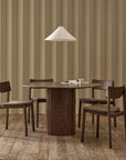 A minimalist dining room with the Wooden Stories Tathra Round Dining Table (stone top), four matching chairs, a white pendant lamp above, and a textured beige wall behind, viewed through open double doors. A cup and an open book rest on the table.