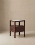 The Theo Nightstand by Wooden Stories features minimalist Danish lines with a square top, open shelf, and closed drawer, set against a neutral beige background—ideal for Natadora or Tolv-inspired interiors.