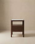 The Theo Nightstand by Wooden Stories features a minimalist, contemporary design with Danish-inspired lines, a rectangular white tabletop, open shelf, and single drawer, shown against a neutral beige background.