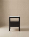 The Theo Nightstand by Wooden Stories is a minimalist wooden side table with Danish-inspired lines, a dark finish, rectangular shape, open shelf, and light top, shown against a beige background.