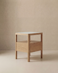 The Theo Nightstand by Wooden Stories is a modern wood side table with Danish lines, featuring a square marble top and one drawer, shown on a neutral beige background.
