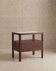 The Theo Nightstand Wide by Wooden Stories, a modern wooden side table with Danish lines, features a drawer and open shelf, and stands on four legs against a neutral beige background.