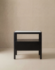 The Theo Nightstand Wide by Wooden Stories is a modern, minimalist black piece featuring Danish lines, a white tabletop, an open shelf, and a lower drawer, showcased against a plain beige background.