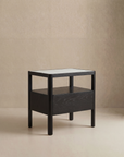 The Theo Nightstand Wide by Wooden Stories is a modern, minimalist black wooden side table featuring clean Danish lines, a rectangular top, and an open shelf, shown against a neutral beige background.