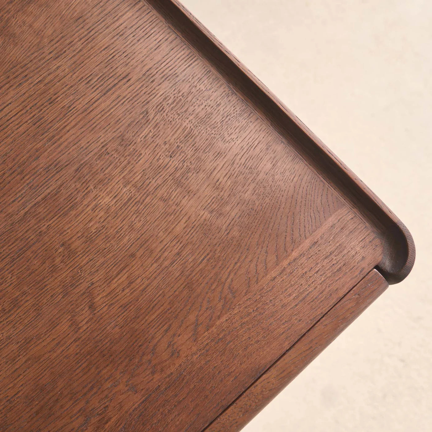 A close-up of the corner of the Wooden Stories Nell Console | Espresso Oak highlights its Danish lines, raised edge, rich wood grain, and smooth finish against a light, neutral background.
