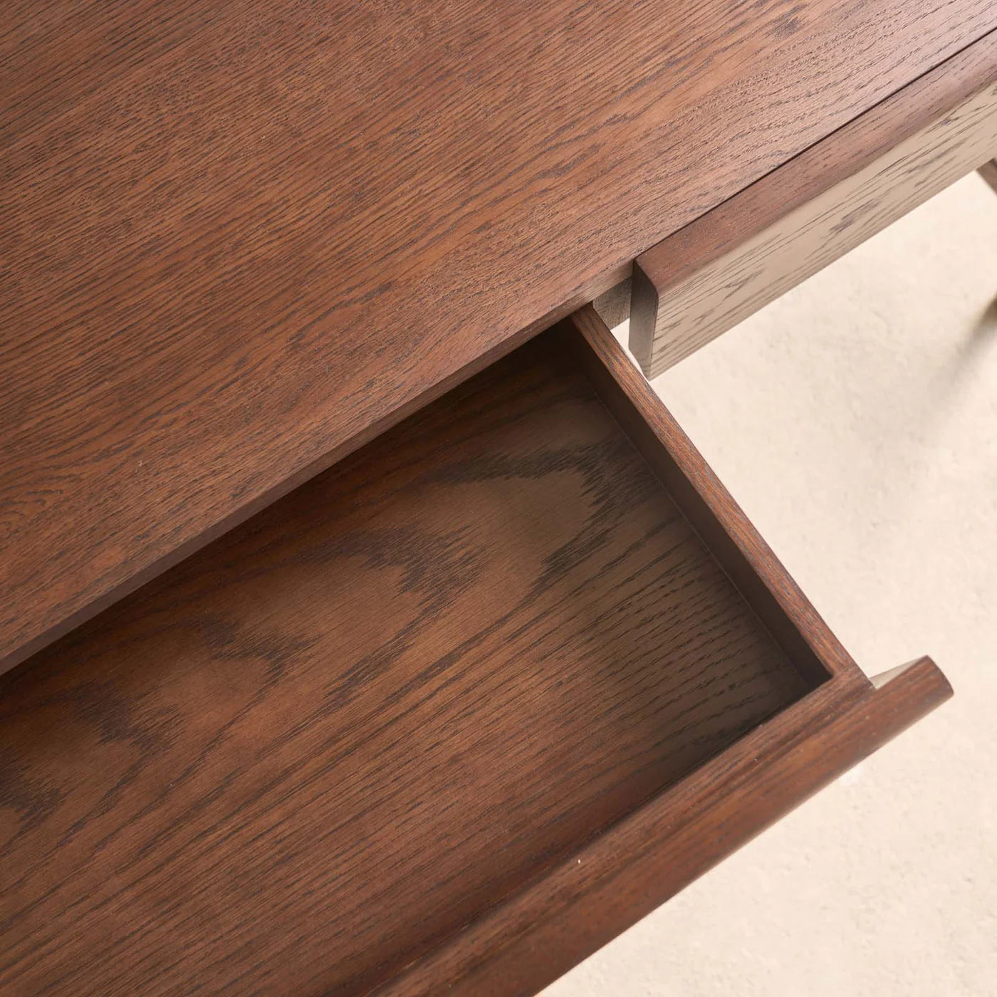 A close-up of the Nell Console by Wooden Stories in Espresso Oak shows a single partially open drawer. The rich brown wood grain and smooth finish create a unified texture and color across the desk and drawer.