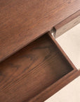 A close-up of the Nell Console by Wooden Stories in Espresso Oak shows a single partially open drawer. The rich brown wood grain and smooth finish create a unified texture and color across the desk and drawer.