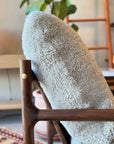 A close-up of SOBU’s Viking Lounge Chair – Walnut with a wooden frame and cream sherpa-style fabric. In the background: a potted plant, wooden ladder, and patterned rug showcase signature SOBU style.