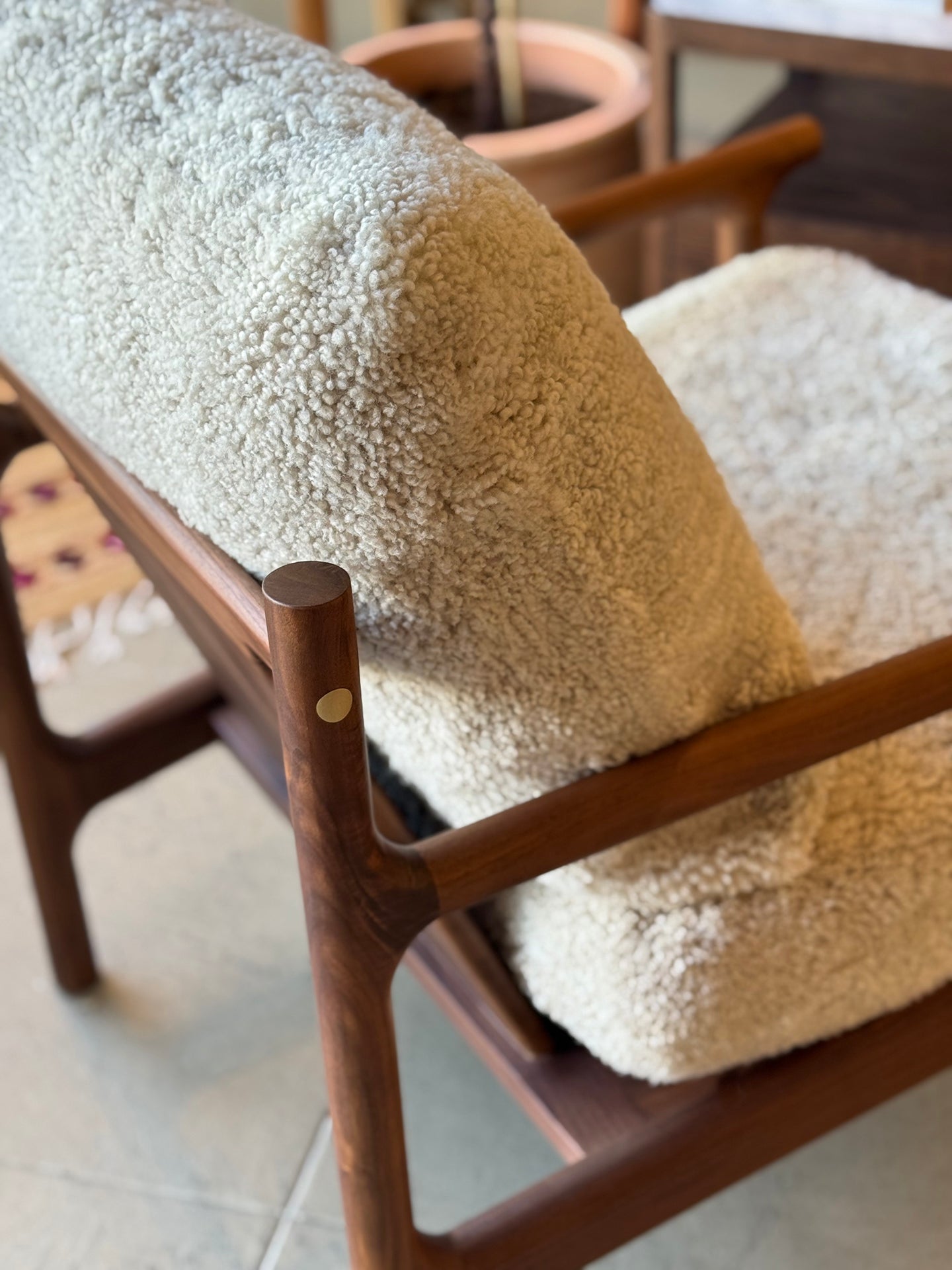 A close-up of the SOBU Viking Lounge Chair - Walnut, featuring smooth, rounded solid walnut and plush cream textured cushions, with cozy upholstery highlighted in a sunlit room.