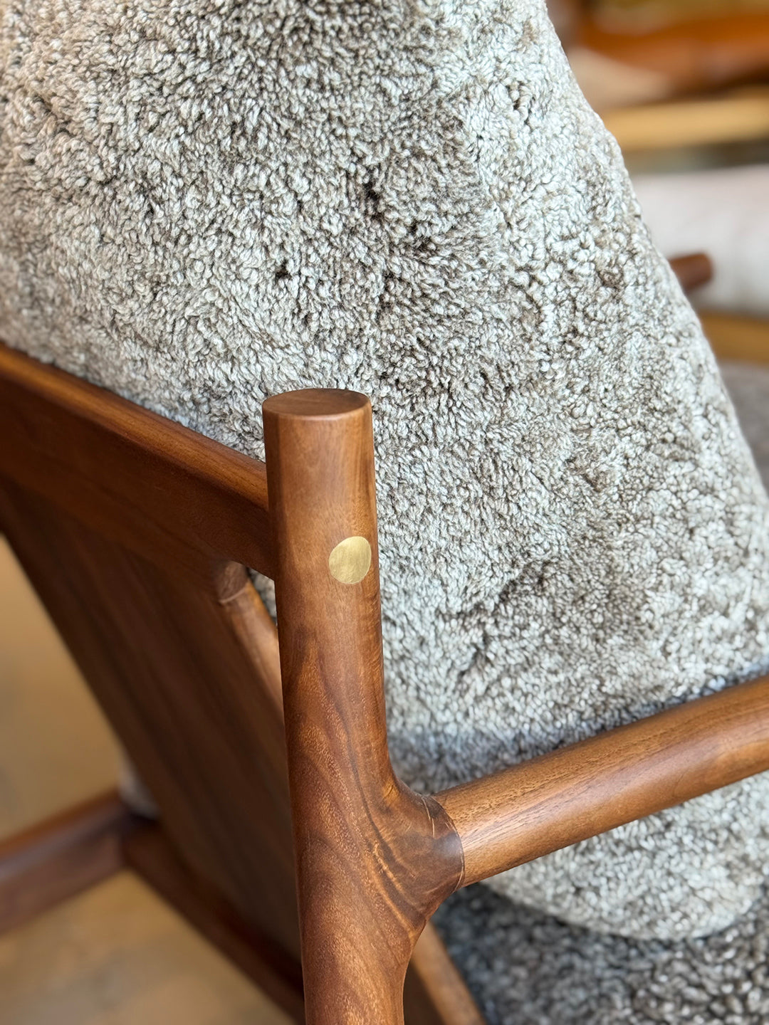 Close-up of the SOBU Viking Lounge Chair - Walnut, showcasing its solid walnut frame with a smooth finish, brass accent, and textured light gray upholstery.