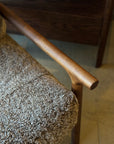 Close-up of a wooden armrest on the Viking Lounge Chair - Walnut by SOBU, featuring a textured brown boucle fabric cushion. Another SOBU furniture piece is partially visible in the background.